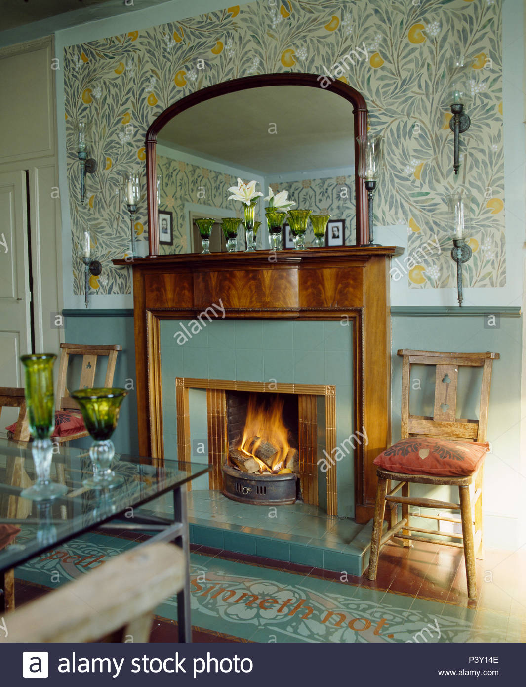 stencilled artscrafts pattern on wall above fireplace with lighted fire in country dining room P3Y14E