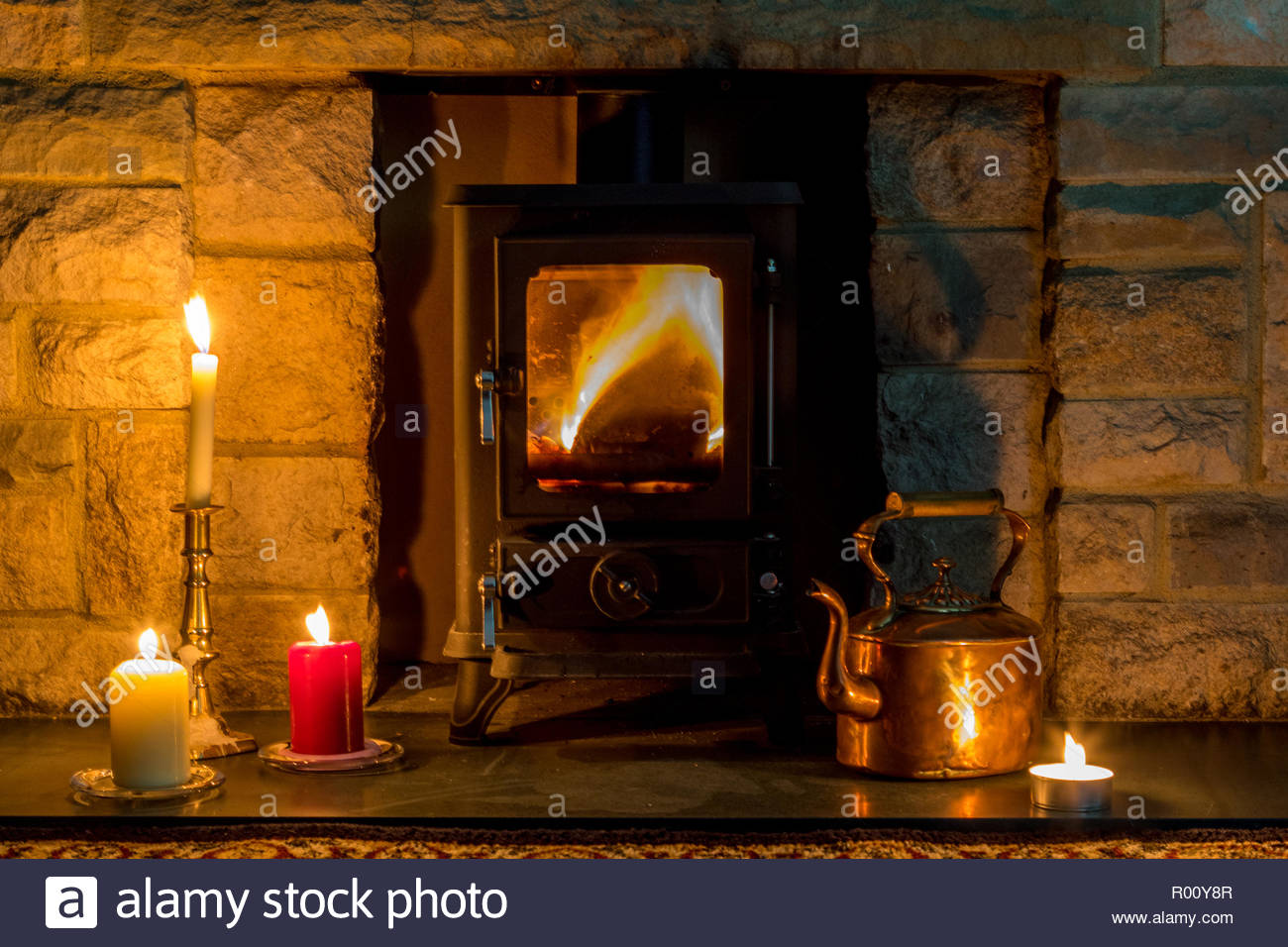 hygge concept a log burner candles and a copper kettle in a stone fireplace R00Y8R