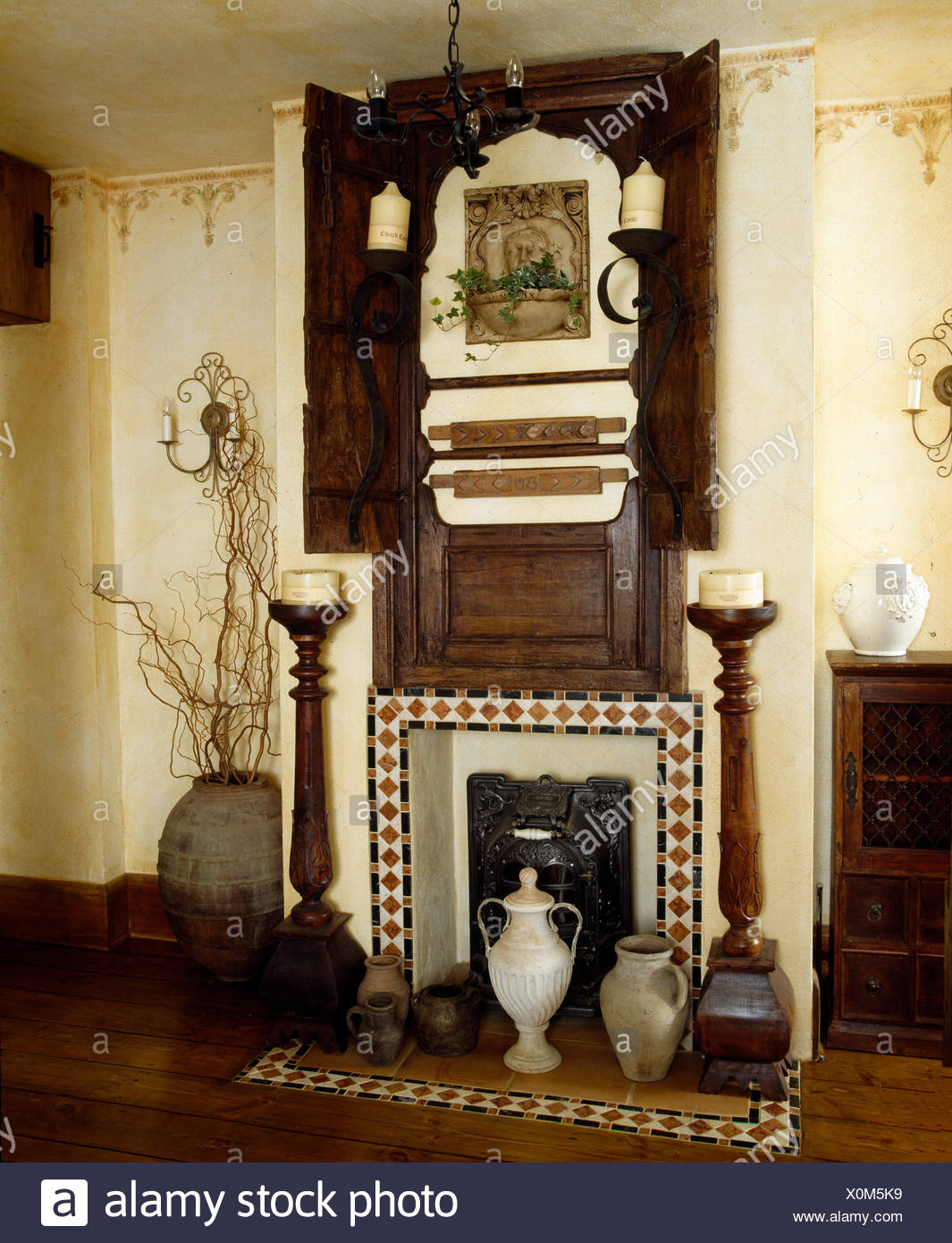 fireplace with old wooden carving above and tall wooden candle holders either side X0M5K9
