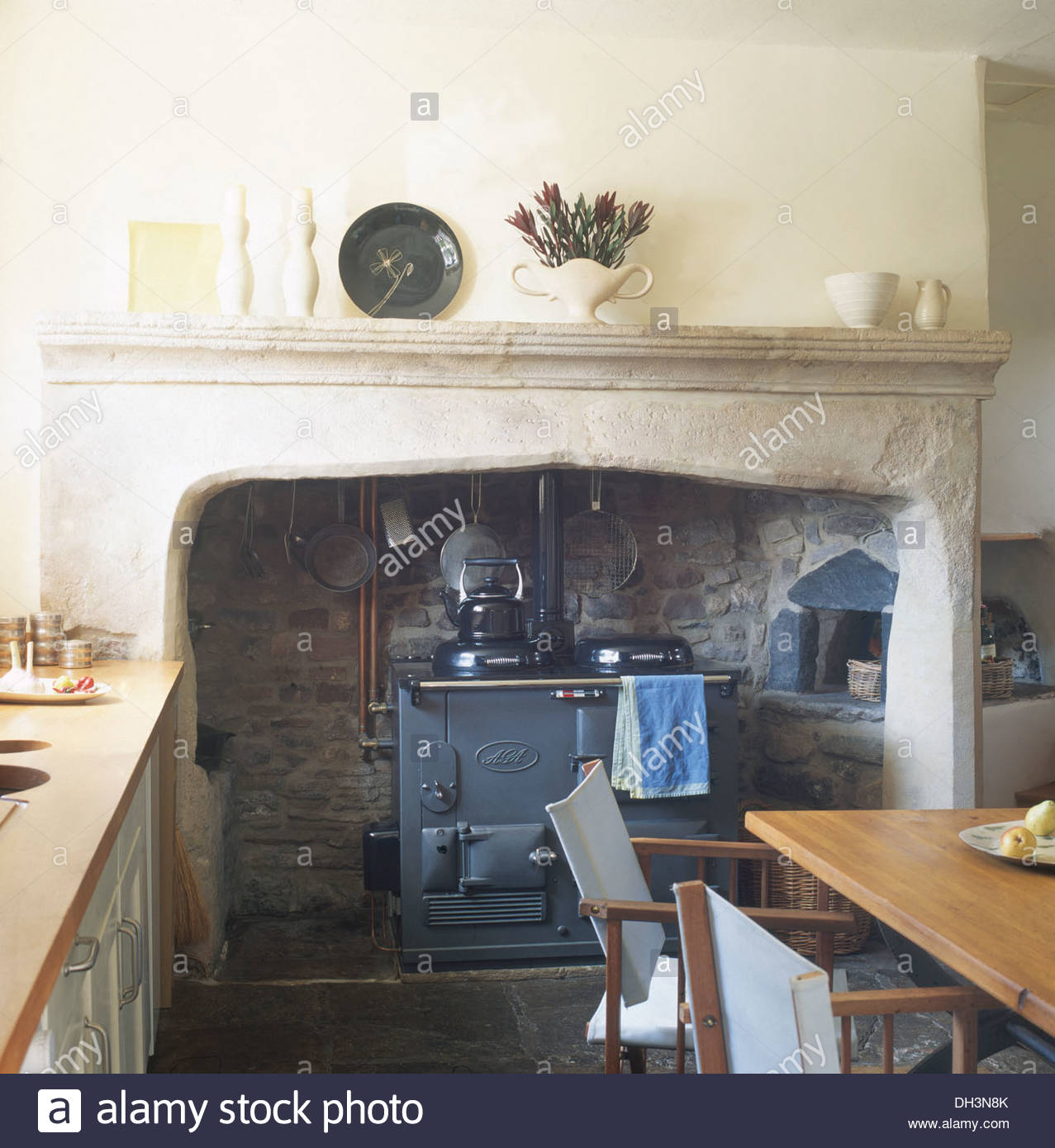 aga oven in stone fireplace in country kitchen with directors chairs DH3N8K