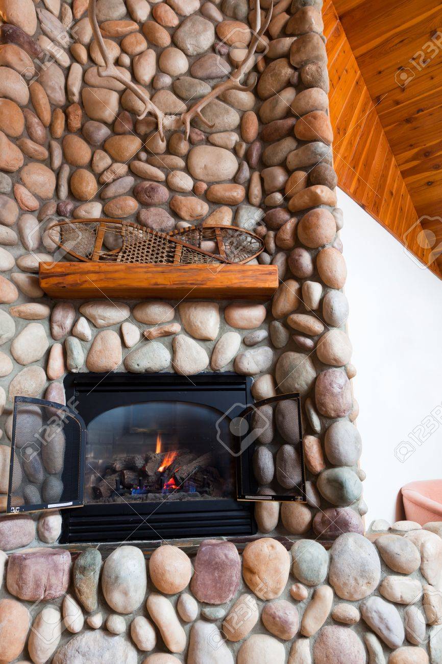 photo a gas fireplace set in colorful river rocks with a wooden mantle topped with vintage snowshoes and l